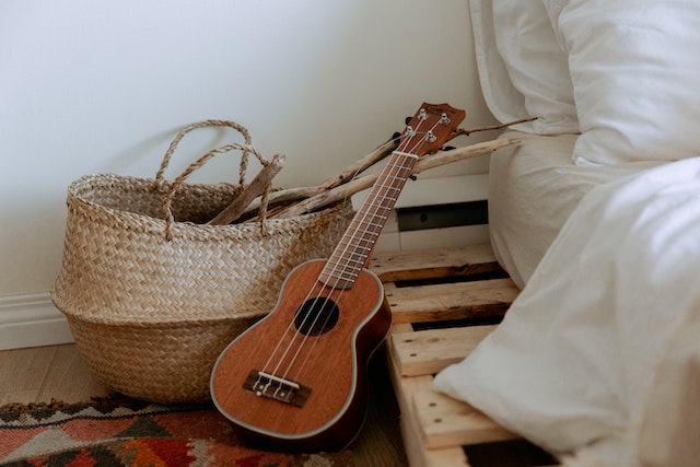 Eine Gitarre kleine, links neben einem Bett angelehnt. Fismoll Gitarre, A7 Gitarre oder andere Akkorde sind damit leider unmöglichn zu spielen, da das Modell nur 4 Saiten aufweist.