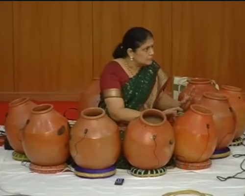 ghatam Eine Frau steht vor einer ganzen Reihe von Ghatam-Instrumenten.